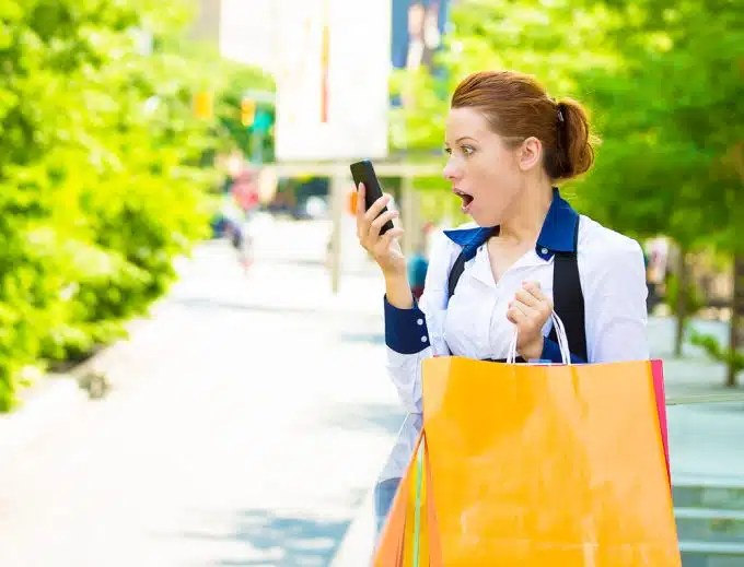Shocked shopper woman looking at her smart phone